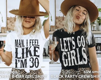 May include: Two women wearing cowboy hats and graphic t-shirts. The white t-shirt says "Man, I feel like I'm 30". The black t-shirt says "Let's go girls".