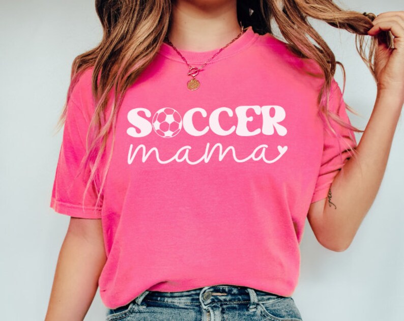May include: A pink t-shirt with the text "SOCCER mama" in white with a white soccer ball graphic.
