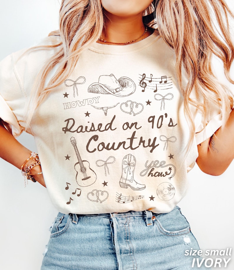May include: Ivory-colored t-shirt with a country music theme. The shirt features a graphic design with a cowboy hat, guitar, musical notes, and the text "Raised on 90's Country". The shirt is size small.