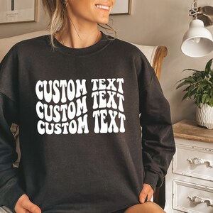 Pu&ograve; includere: Felpa nera con la scritta "CUSTOM TEXT" in un carattere bianco ondulato, impilata tre volte. Un capo casual per l'uso quotidiano.