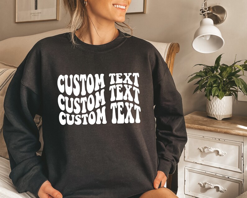 Pu&ograve; includere: Felpa nera con la scritta "CUSTOM TEXT" in un carattere bianco ondulato, impilata tre volte. Un capo casual per l'uso quotidiano.