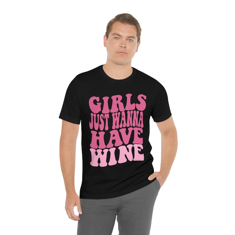 Peut inclure: Un t-shirt noir avec un motif rose et blanc qui dit "Girls Just Wanna Have Wine".