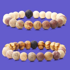 May include: Two beaded bracelets with brown, white, and black beads. The bracelets have a lava rock bead in the center.