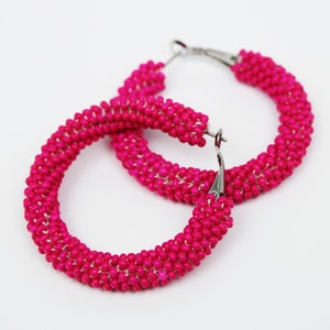 Könnte beinhalten: Ein Paar rosafarbene Perlen-Creolen. Die Ohrringe bestehen aus kleinen, runden Perlen, die zu einer Creolenform zusammengefügt sind. Die Creolen haben einen Durchmesser von etwa 5 cm.