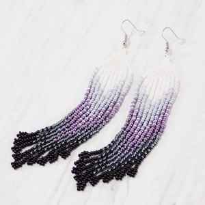 May include: A pair of long, beaded earrings with a gradient of purple, gray, and white beads. The earrings have silver hooks.