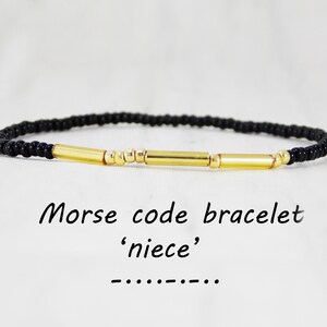 May include: Black beaded bracelet with gold beads and bars spelling out 'niece' in Morse code. Morse code bracelet 'niece'.