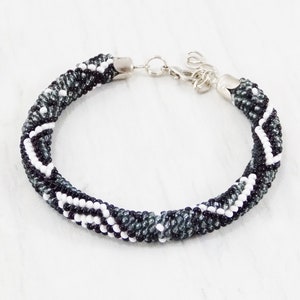 May include: A black, white, and gray beaded bracelet with a silver clasp.