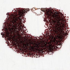 May include: A red beaded necklace with a delicate chain closure. The necklace is made of many strands of small, red beads, creating a full and layered look.