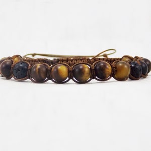 Pode incluir: Um bracelete trançado castanho com contas de olho de tigre e lava negra.