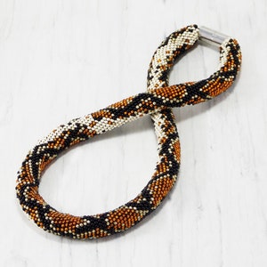 Peut inclure: Un collier de perles avec un motif de peau de serpent en noir, blanc et or.