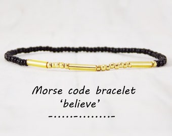 May include: A black beaded bracelet with gold beads and two gold bars. The bracelet spells out the word 'believe' in Morse code.