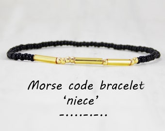 May include: Black beaded bracelet with gold beads and bars spelling out 'niece' in Morse code. Morse code bracelet 'niece'.
