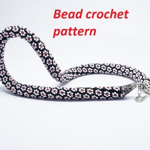 May include: A black and white beaded necklace with red accents, featuring a flower pattern. The necklace is made with small beads and has a silver clasp. Bead crochet pattern.