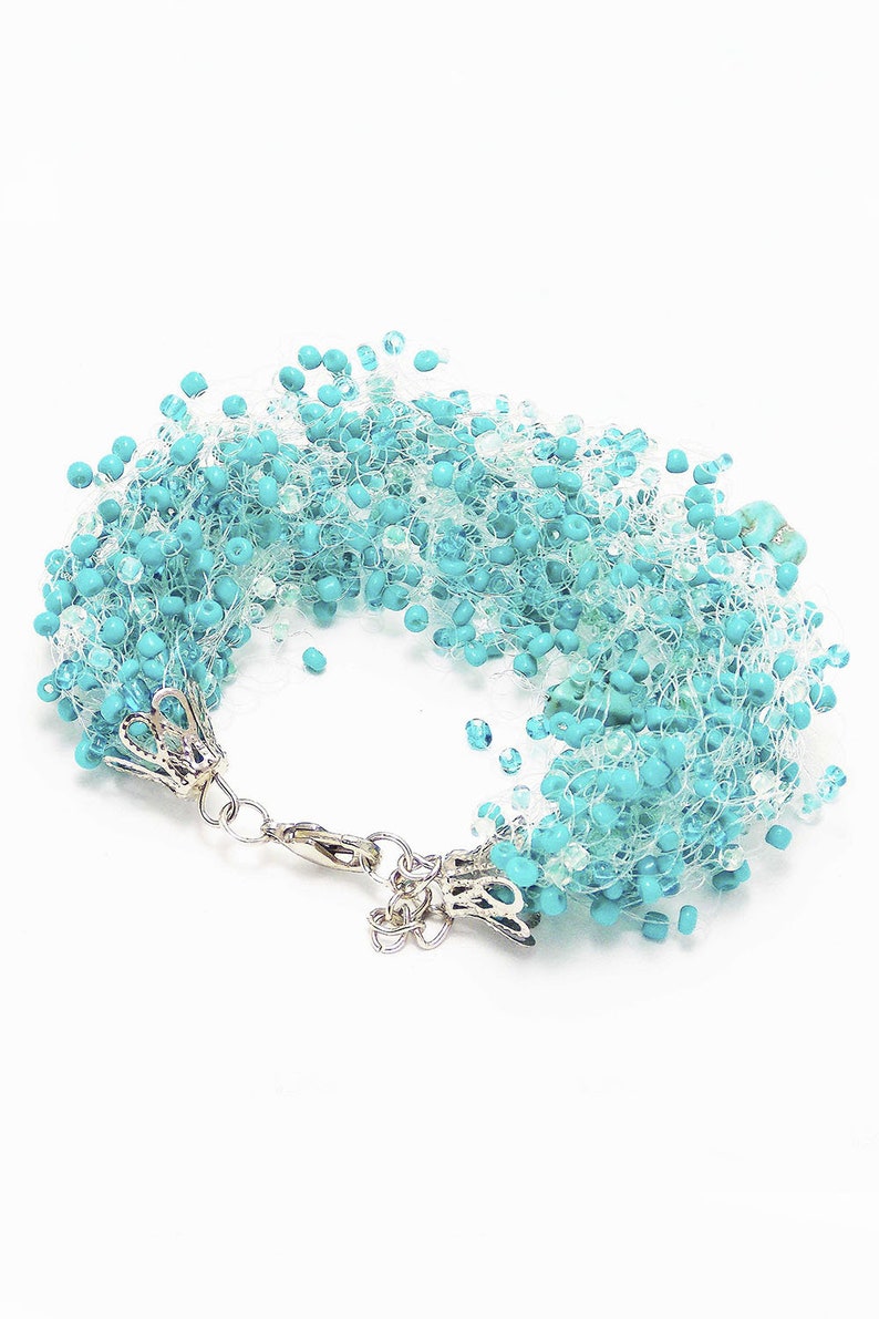 May include: A turquoise beaded bracelet with a silver clasp. The beads are strung on a white thread and create a fluffy, layered effect.