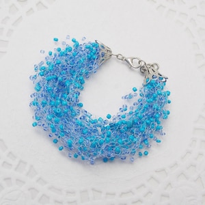 May include: A blue and white beaded bracelet with a silver clasp. The beads are small and create a cascading effect.