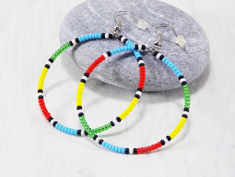 May include: A pair of colorful beaded hoop earrings with a black, white, red, yellow, and green color scheme. The earrings are made with small beads and have a silver hook closure.