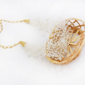 May include: A gold chain necklace with a woven basket-like pendant filled with white beads and crystals.