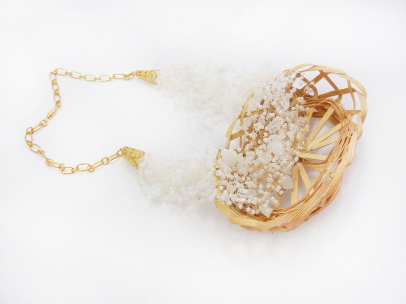 May include: A gold chain necklace with a woven basket-like pendant filled with white beads and crystals.
