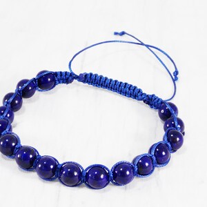 May include: A blue beaded bracelet with a knotted cord closure. The beads are round and have a dark blue color.