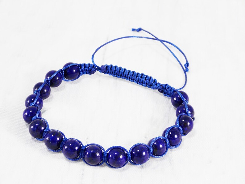 May include: A blue beaded bracelet with a knotted cord closure. The beads are round and have a dark blue color.