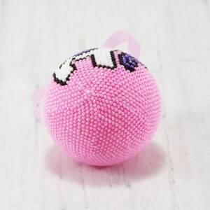 May include: Pink beaded Christmas ornament with a white and purple unicorn design.