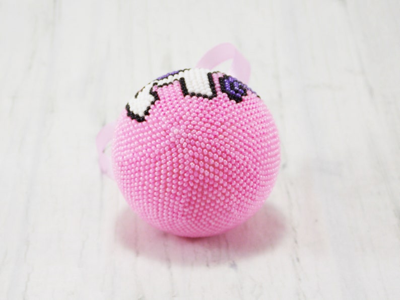 May include: Pink beaded Christmas ornament with a white and purple unicorn design.