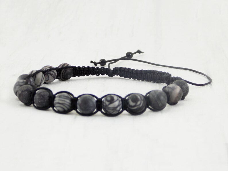 Puede incluir: Un brazalete trenzado negro con cuentas de patrones grises y blancos.