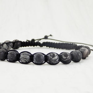 Puede incluir: Un brazalete trenzado negro con cuentas de patrones grises y blancos.