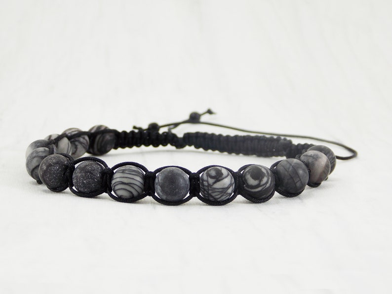 Puede incluir: Un brazalete trenzado negro con cuentas de patrones grises y blancos.