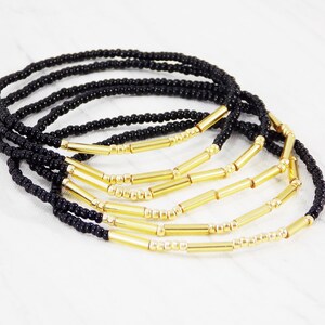 May include: A set of black and gold beaded bracelets. The bracelets are made with small black beads and gold bar beads.