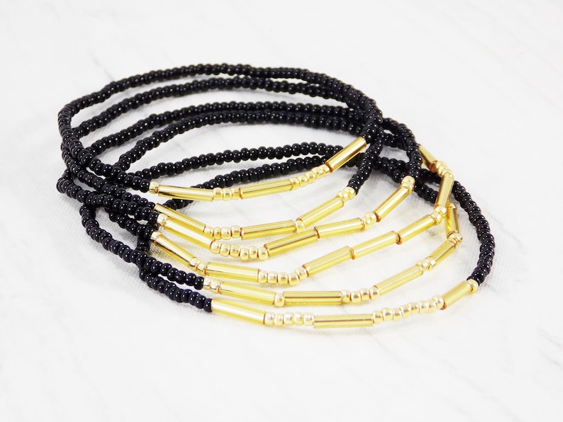May include: A set of black and gold beaded bracelets. The bracelets are made with small black beads and gold bar beads.