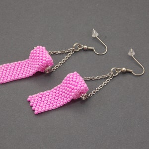May include: A pair of pink beaded earrings with a rolled design and silver chains. The earrings have silver hooks.