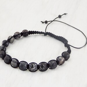 Puede incluir: Un brazalete de cord&oacute;n negro con cuentas rayadas en blanco y negro.