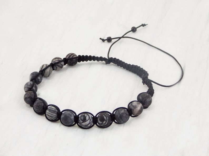 Puede incluir: Un brazalete de cord&oacute;n negro con cuentas rayadas en blanco y negro.