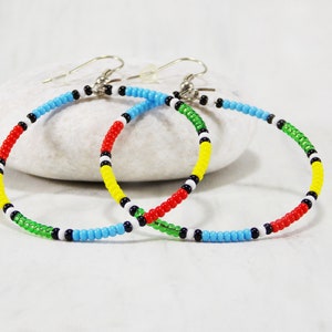 May include: A pair of colorful beaded hoop earrings with red, yellow, green, blue, white, and black beads. The earrings are made with silver hooks.