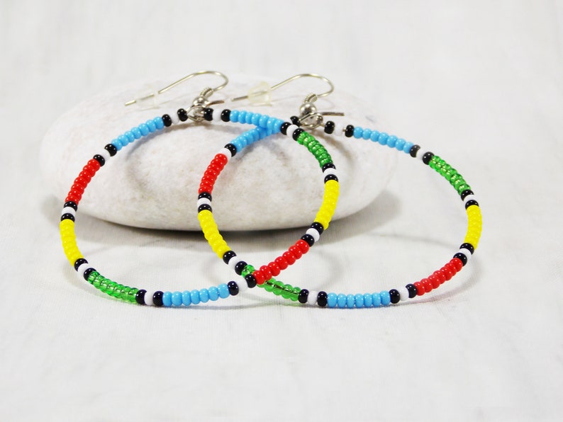 May include: A pair of colorful beaded hoop earrings with red, yellow, green, blue, white, and black beads. The earrings are made with silver hooks.