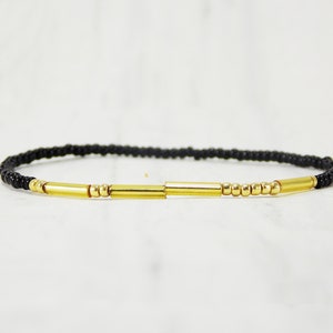 May include: A black beaded bracelet with gold accents. The bracelet features three gold bars and small gold beads.