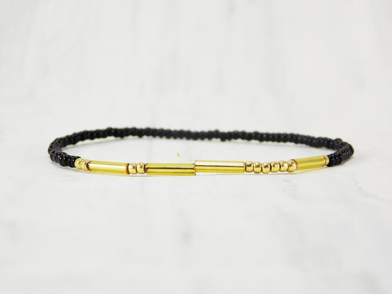 May include: A black beaded bracelet with gold accents. The bracelet features three gold bars and small gold beads.