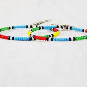 May include: Two colorful beaded bracelets with alternating colors of red, yellow, green, blue, white, and black.