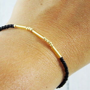 May include: A simple bracelet with black beads and gold spacers. The bracelet is on a person's wrist.