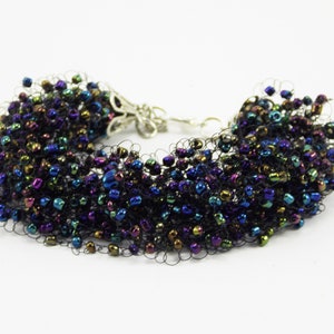 May include: A black beaded bracelet with iridescent beads in shades of blue, green, and purple. The bracelet is made with a stretchy cord and has a silver clasp.