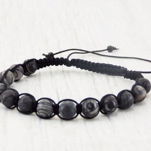 Puede incluir: Un brazalete trenzado negro con cuentas de color gris y blanco con patrones.