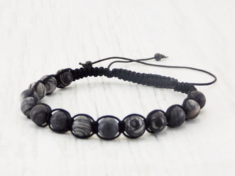 Puede incluir: Un brazalete trenzado negro con cuentas de color gris y blanco con patrones.