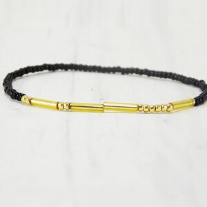 May include: A black beaded bracelet with gold bar accents.