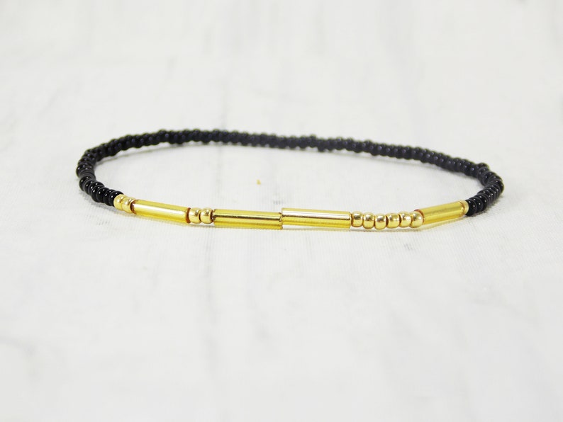 May include: A black beaded bracelet with gold bar accents.