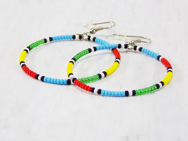 May include: A pair of hoop earrings made with colorful beads. The beads are red, yellow, green, blue, black, and white. The earrings are made with a silver wire.