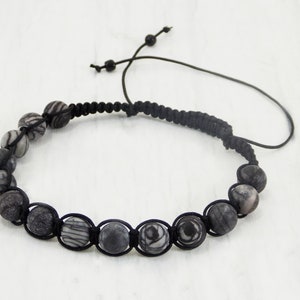 Puede incluir: Pulsera de cuentas de piedra rayadas en blanco y negro con un cord&oacute;n negro. La pulsera tiene un cierre de nudo deslizante.