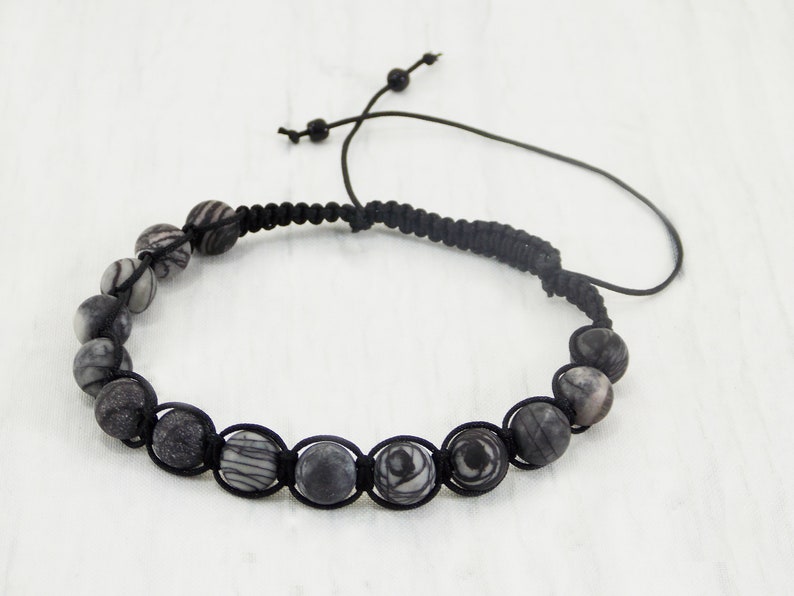 Puede incluir: Pulsera de cuentas de piedra rayadas en blanco y negro con un cord&oacute;n negro. La pulsera tiene un cierre de nudo deslizante.