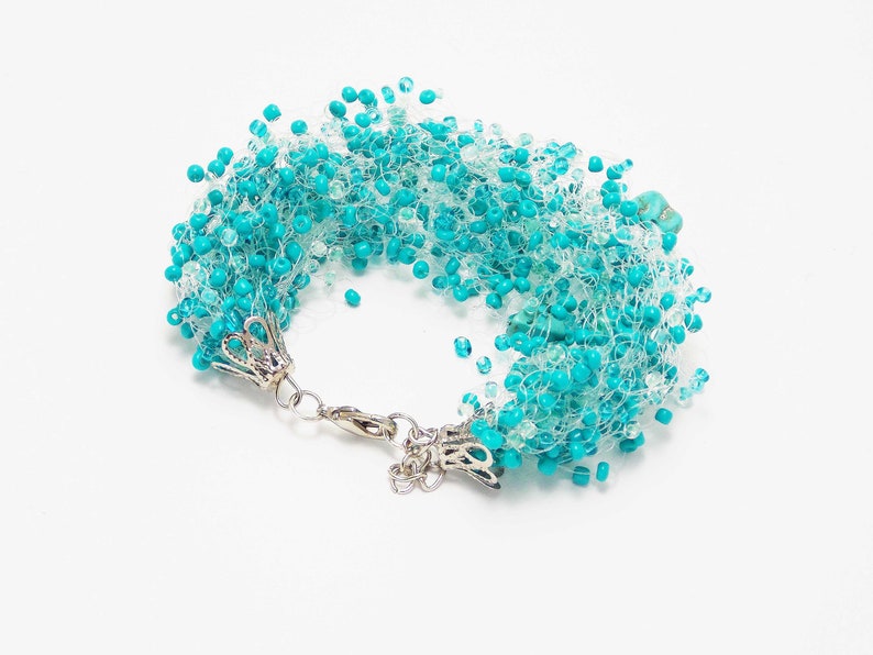 May include: A turquoise and white beaded bracelet with a silver clasp. The beads are arranged in a cascading pattern, creating a unique and eye-catching design.