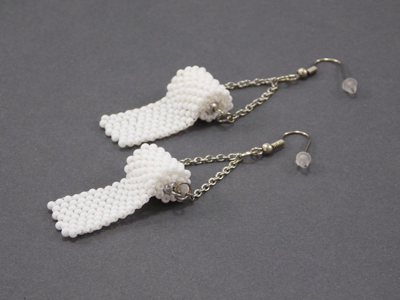 May include: A pair of white beaded earrings shaped like a roll of toilet paper, hanging from silver chains with silver hooks.
